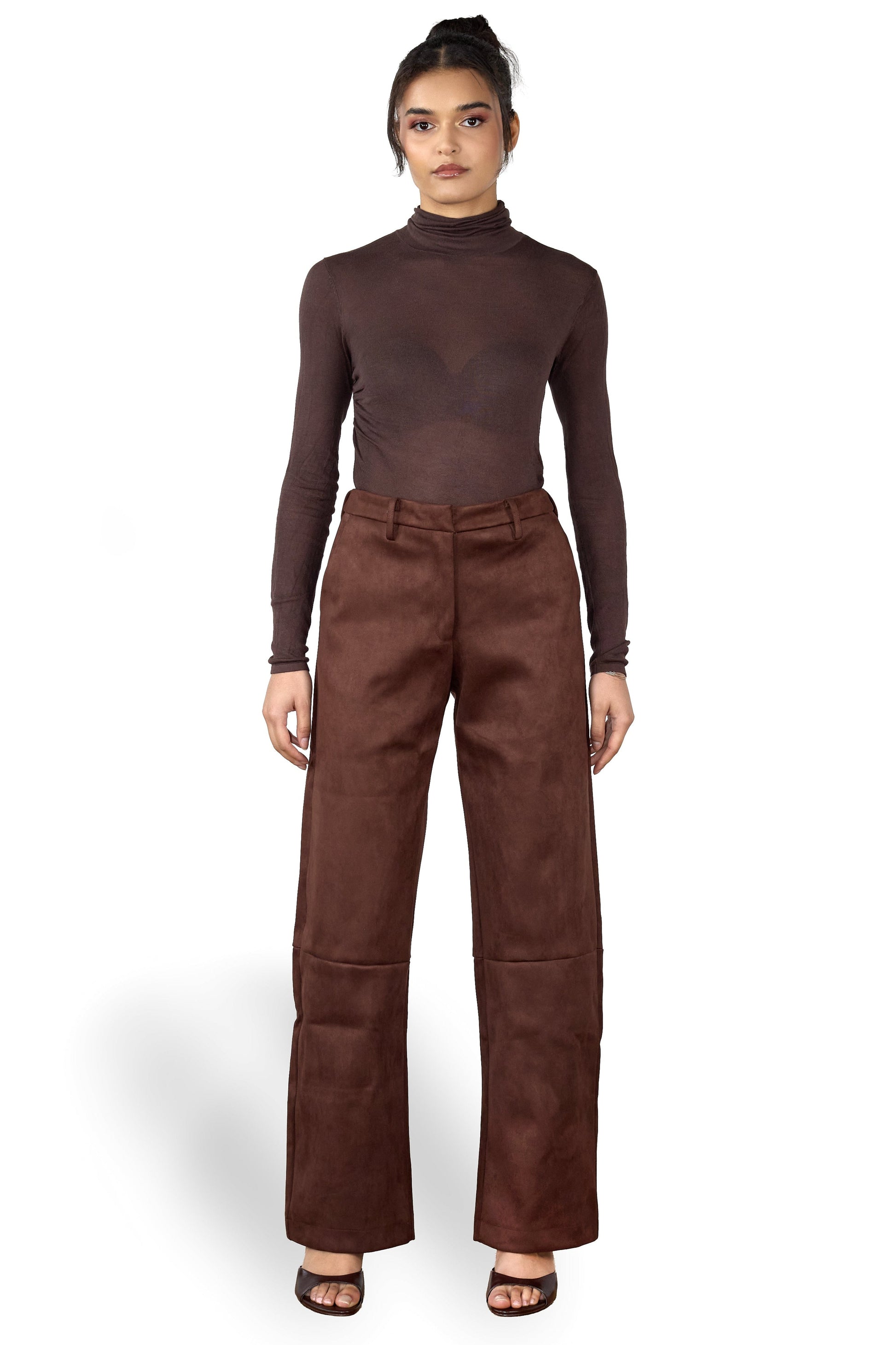 Woman wearing a brown turtleneck and wide-leg brown suede pants on a white background