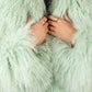 Close-up of a person wearing a light green Mongolian furt with hands adjusting it.
