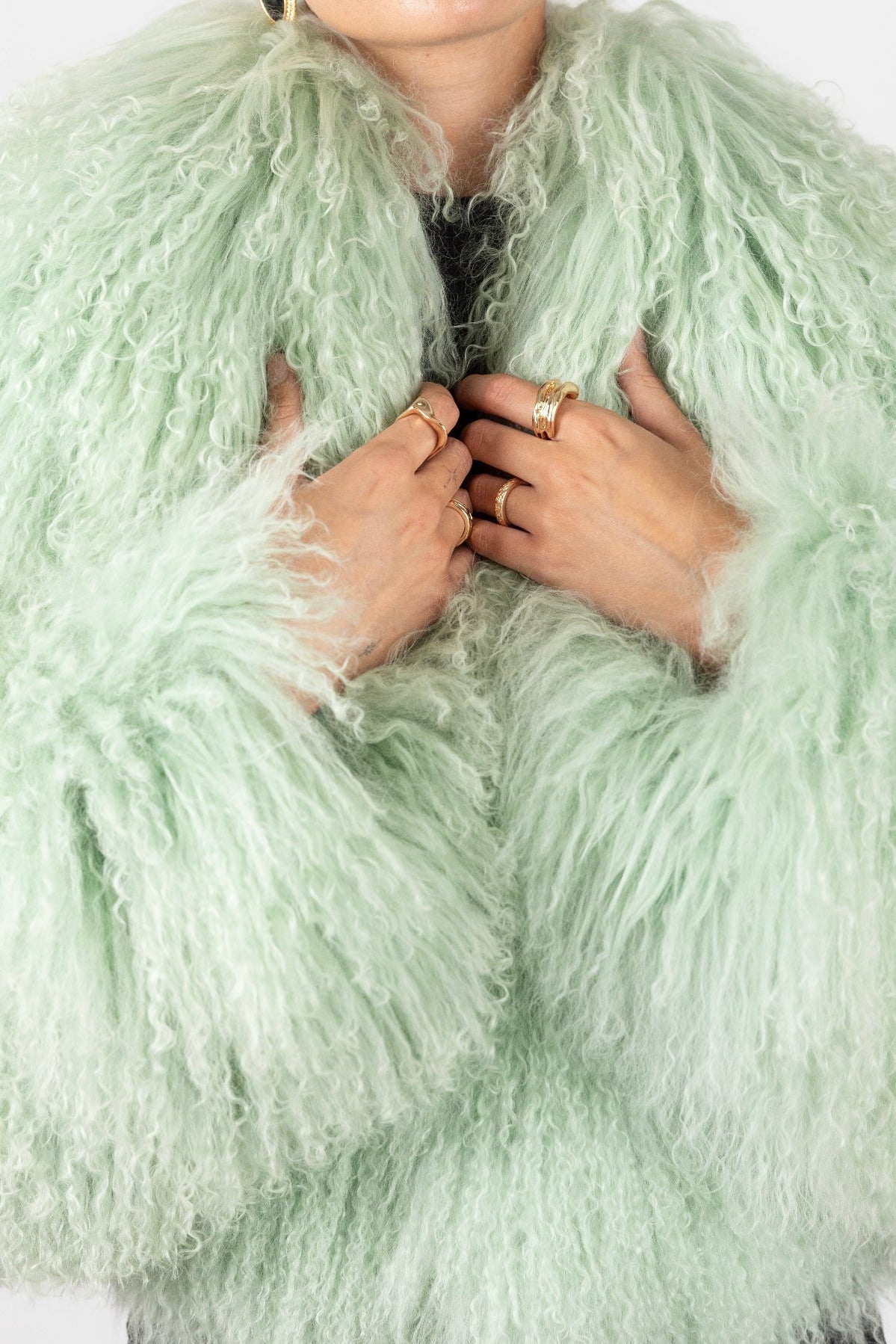 Close-up of a person wearing a light green Mongolian furt with hands adjusting it.