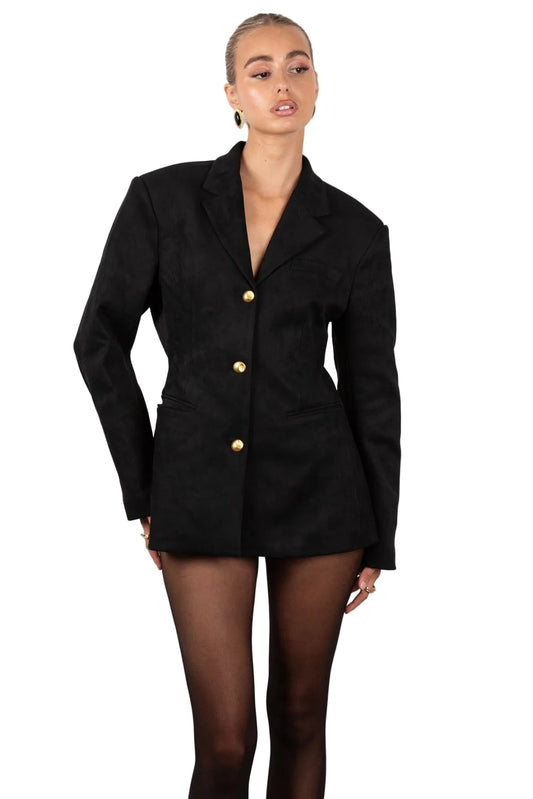 Woman wearing a black blazer with gold buttons on a white background