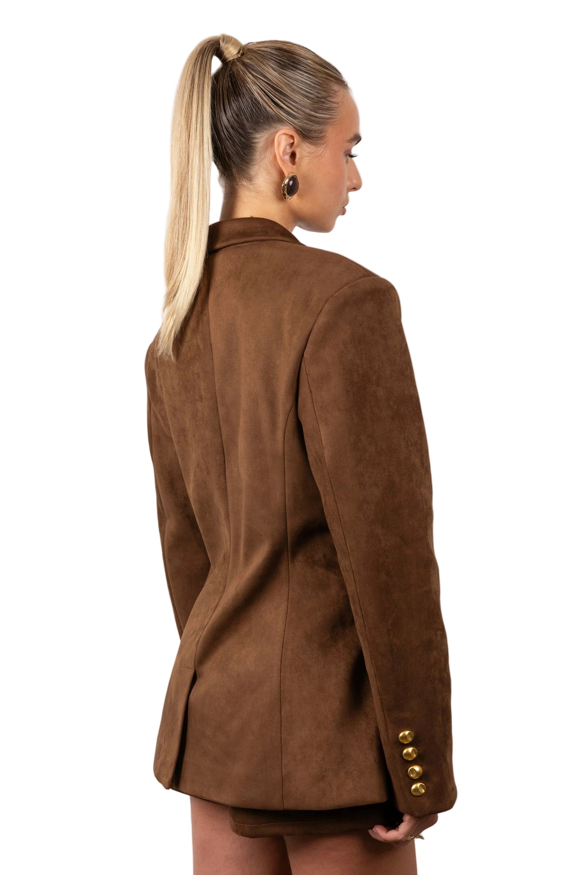 Woman wearing a brown blazer with gold buttons on a white background