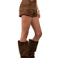 Person wearing brown suede boots, shorts, and top on a plain background