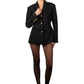 Person wearing a black blazer with gold buttons on a plain background